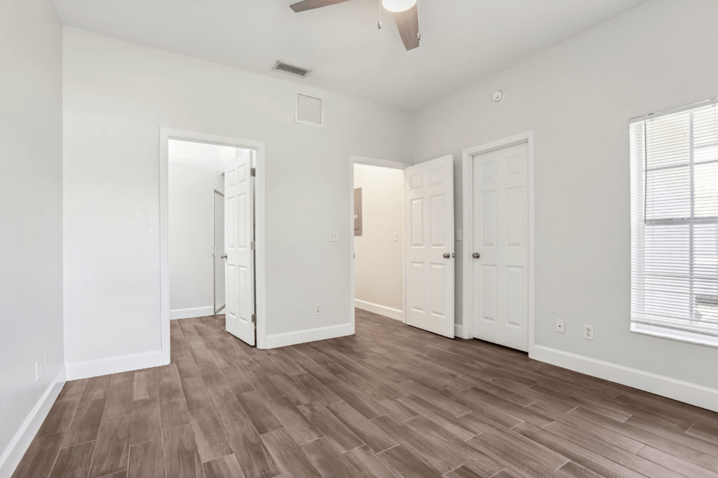 A room with white walls and wood flooring with a ceiling fan.